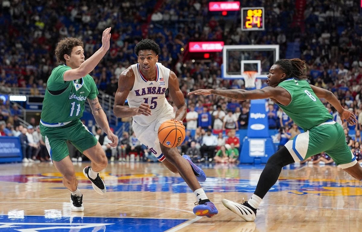 Nov 11, 2025; Lawrence, Kansas, USA; Kansas Jayhawks forward Bryson Tiller (15) drives against Texas A&M-Corpus Christi Islanders forward Jaden Haire (11) and guard Bryson Wheatfall (8) during the second half at Allen Fieldhouse. Mandatory Credit: Jay Biggerstaff-Imagn Images