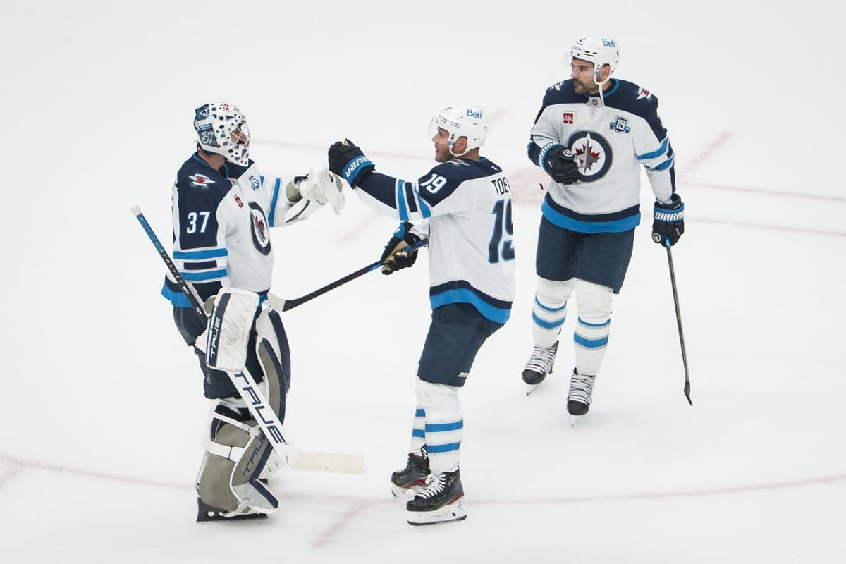 Nov 11, 2025; Vancouver, British Columbia, CAN; Winnipeg Jets goalie Connor Hellebuyck (37) and forward Jonathan Toews (19) and defenseman Dylan DeMelo (2) celebrate their victory against the Vancouver Canucks at Rogers Arena. Mandatory Credit: Bob Frid-Imagn Images