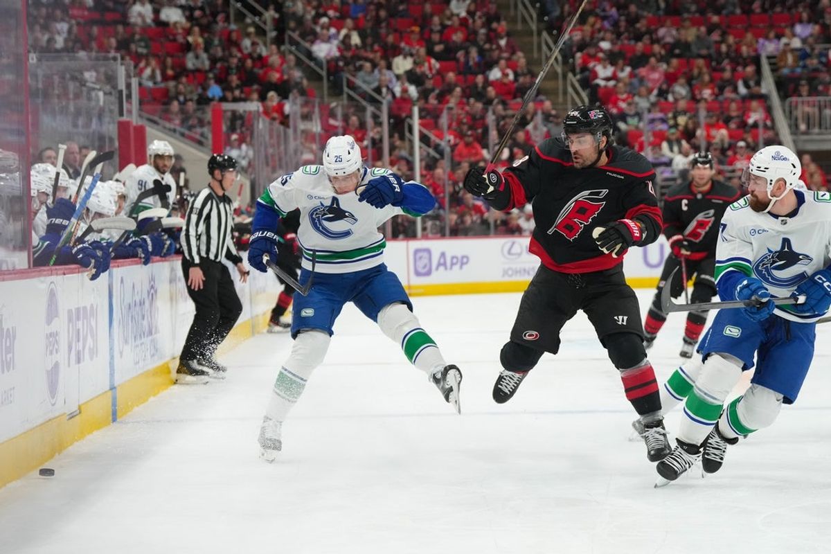 Nov 14, 2025; Raleigh, North Carolina, USA;  Carolina Hurricanes left wing William Carrier (28) is checked by Vancouver Canucks defenseman Elias Pettersson (25) during the first period at Lenovo Center. Mandatory Credit: James Guillory-Imagn Images
