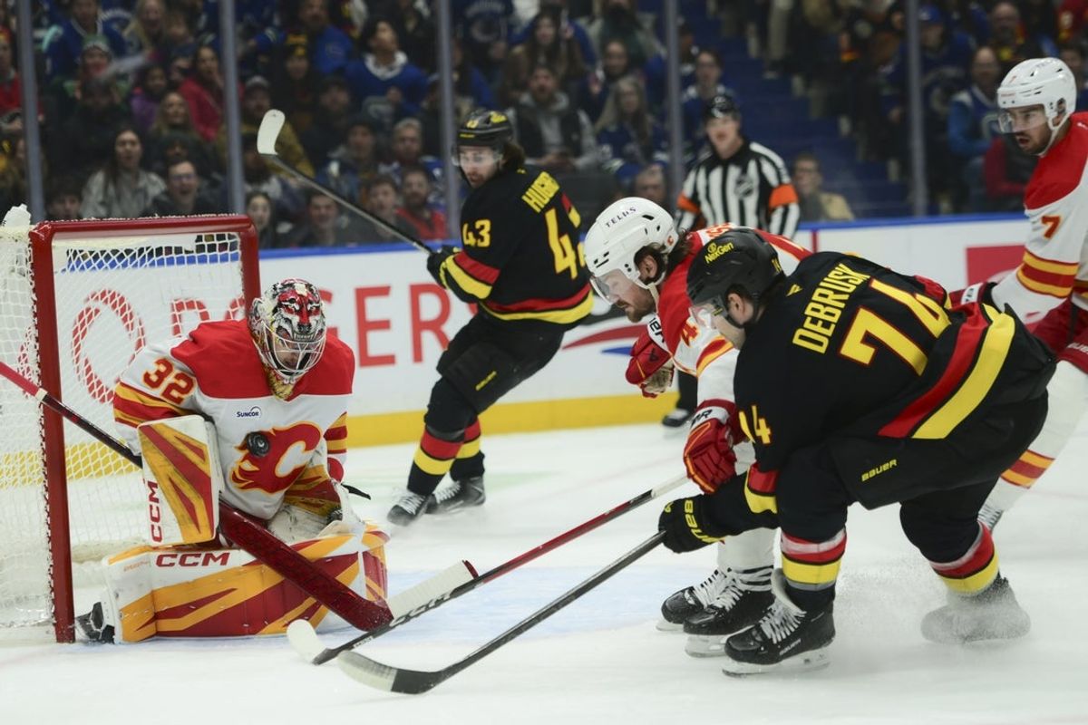 Nov 23, 2025; Vancouver, British Columbia, CAN;  Calgary Flames goaltender Dustin Wolf (32) blocks a shot by Vancouver Canucks left wing Jake Debrusk (74) at Rogers Arena. Mandatory Credit: Simon Fearn-Imagn Images