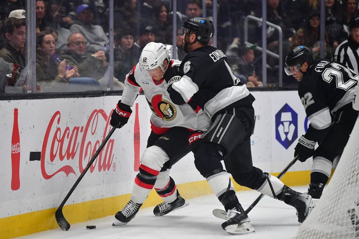 Nov 24, 2025; Los Angeles, California, USA;Los Angeles Kings defenseman Joel Edmundson (6) hits Ottawa Senators center Shane Pinto (12) to the boards while playing for the puck during the first period at Crypto.com Arena. Mandatory Credit: Gary A. Vasquez-Imagn Images