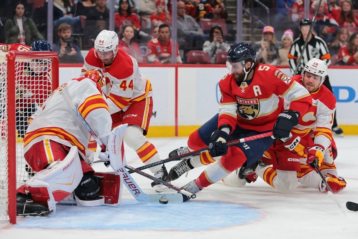 Nov 28, 2025; Sunrise, Florida, USA; Calgary Flames goaltender Devin Cooley (1) makes a save against Florida Panthers defenseman Aaron Ekblad (5) during the third period at Amerant Bank Arena. Mandatory Credit: Sam Navarro-Imagn Images