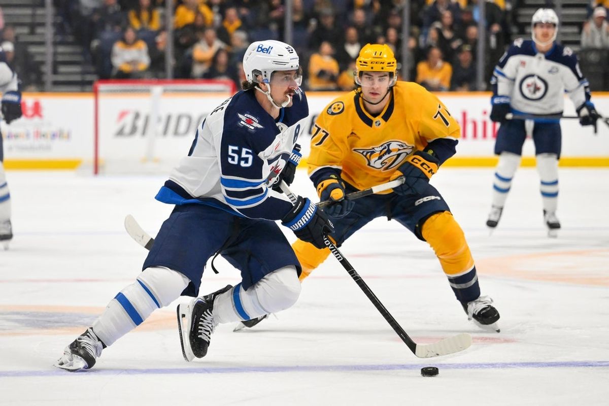 Nov 29, 2025; Nashville, Tennessee, USA;   Winnipeg Jets center Mark Scheifele (55) plays the puck against Nashville Predators right wing Luke Evangelista (77) during the second period at Bridgestone Arena. Mandatory Credit: Steve Roberts-Imagn Images