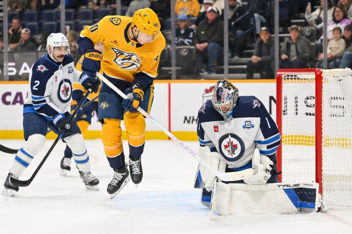 Nov 29, 2025; Nashville, Tennessee, USA;  Nashville Predators center Fedor Svechkov (40) deflects the puck as Winnipeg Jets goaltender Eric Comrie (1) blocks it during the third period at Bridgestone Arena. Mandatory Credit: Steve Roberts-Imagn Images