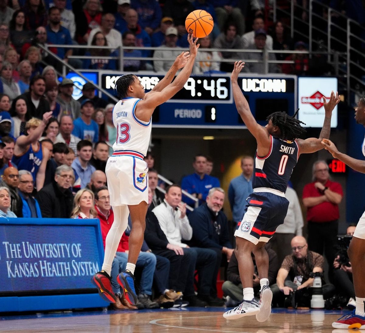 Dec 2, 2025; Lawrence, Kansas, USA; Kansas Jayhawks guard Elmarko Jackson (13) shoots a three point basket as UConn Huskies guard Malachi Smith (0) defends during the first half of the game at Allen Fieldhouse. Mandatory Credit: Denny Medley-Imagn Images