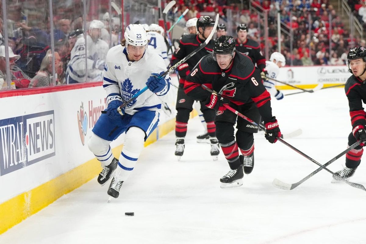 Dec 4, 2025; Raleigh, North Carolina, USA; Toronto Maple Leafs left wing Matthew Knies (23) skates with the puck past Carolina Hurricanes defenseman Mike Reilly (6) during the second period at Lenovo Center. Mandatory Credit: James Guillory-Imagn Images