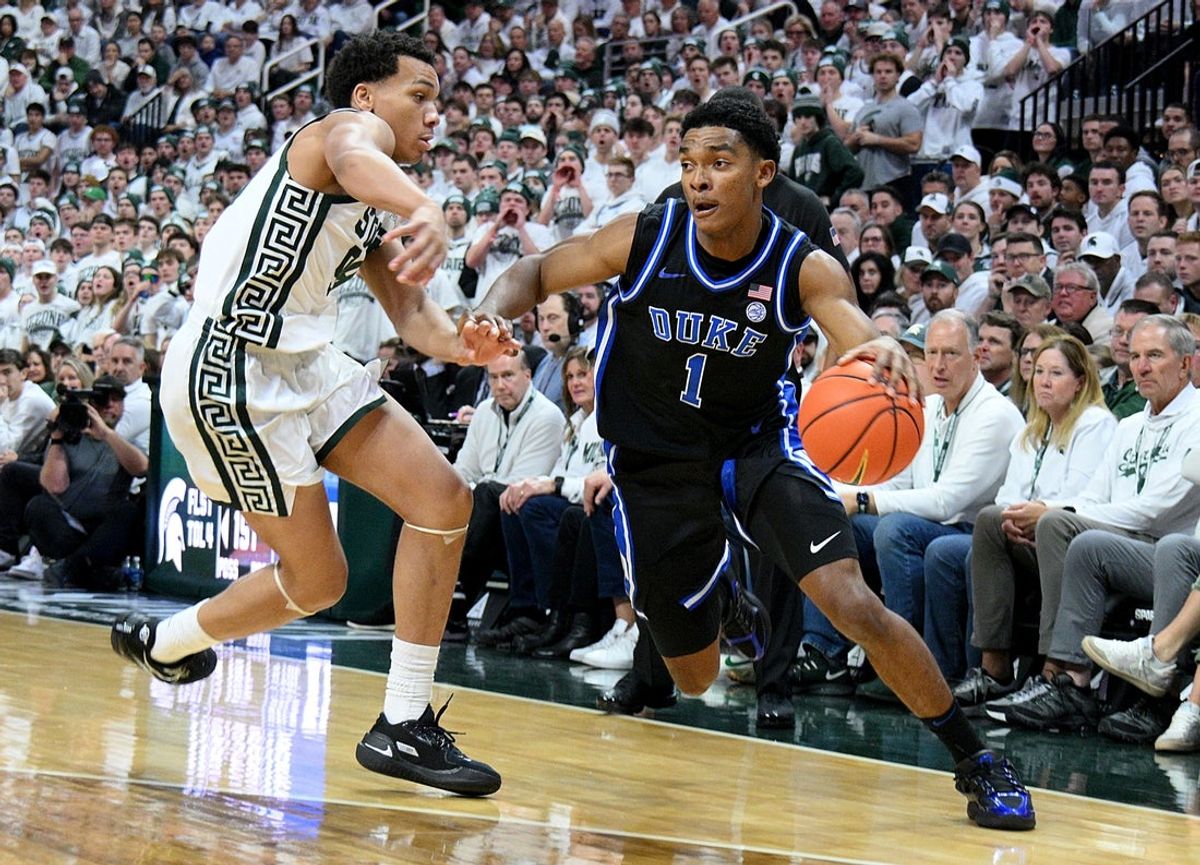 Dec 6, 2025; East Lansing, Michigan, USA;  Duke Blue Devils guard Caleb Foster (1) dribbles past Michigan State Spartans guard Divine Ugochukwu (99) during the first half at Jack Breslin Student Events Center. Mandatory Credit: Dale Young-Imagn Images