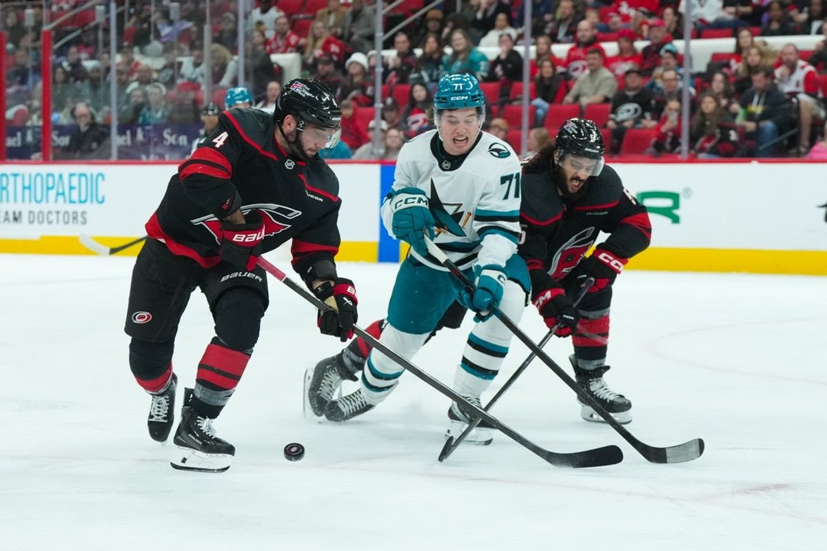 Dec 7, 2025; Raleigh, North Carolina, USA;  Carolina Hurricanes defenseman Shayne Gostisbehere (4)  defenseman Jalen Chatfield (5) and San Jose Sharks center Macklin Celebrini (71) battle over the puck during the second period at Lenovo Center. Mandatory Credit: James Guillory-Imagn Images