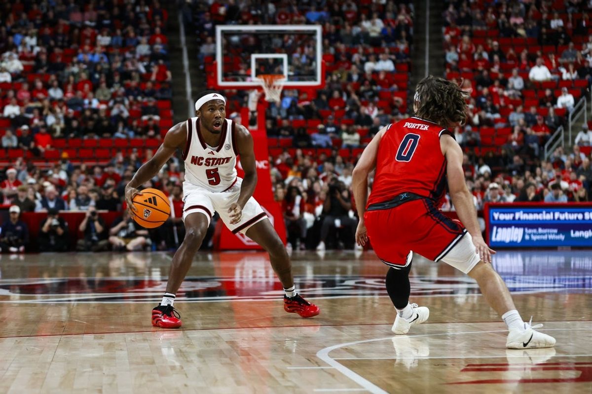 Dec 6, 2025; Raleigh, North Carolina, USA; NC State Wolfpack guard Tre Holloman (5) dribbles with the ball guarded by Liberty Flames guard Colin Porter (0) during the first half of the game at Lenovo Center. Mandatory Credit: Jaylynn Nash-Imagn Images