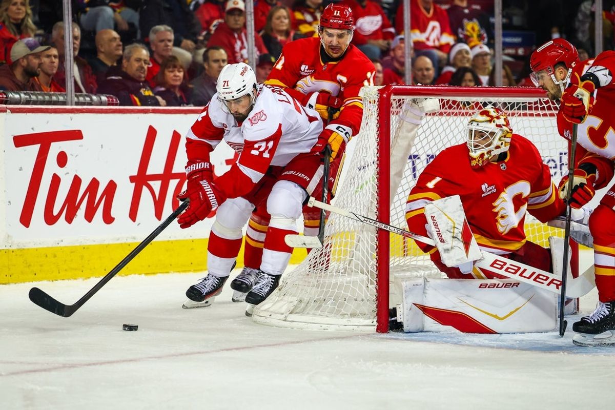 Dec 10, 2025; Calgary, Alberta, CAN; Detroit Red Wings center Dylan Larkin (71) and Calgary Flames center Mikael Backlund (11) battle for the puck behind the net of Calgary Flames goaltender Devin Cooley (1) during the first period at Scotiabank Saddledome. Mandatory Credit: Sergei Belski-Imagn Images
