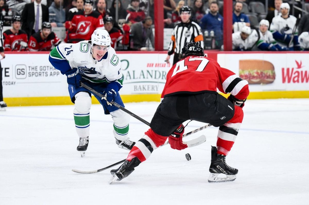 Dec 14, 2025; Newark, New Jersey, USA; Vancouver Canucks defenseman Zeev Buium (24) skates with the puck while defended by New Jersey Devils left wing Paul Cotter (47) during the first period at Prudential Center. Mandatory Credit: John Jones-Imagn Images