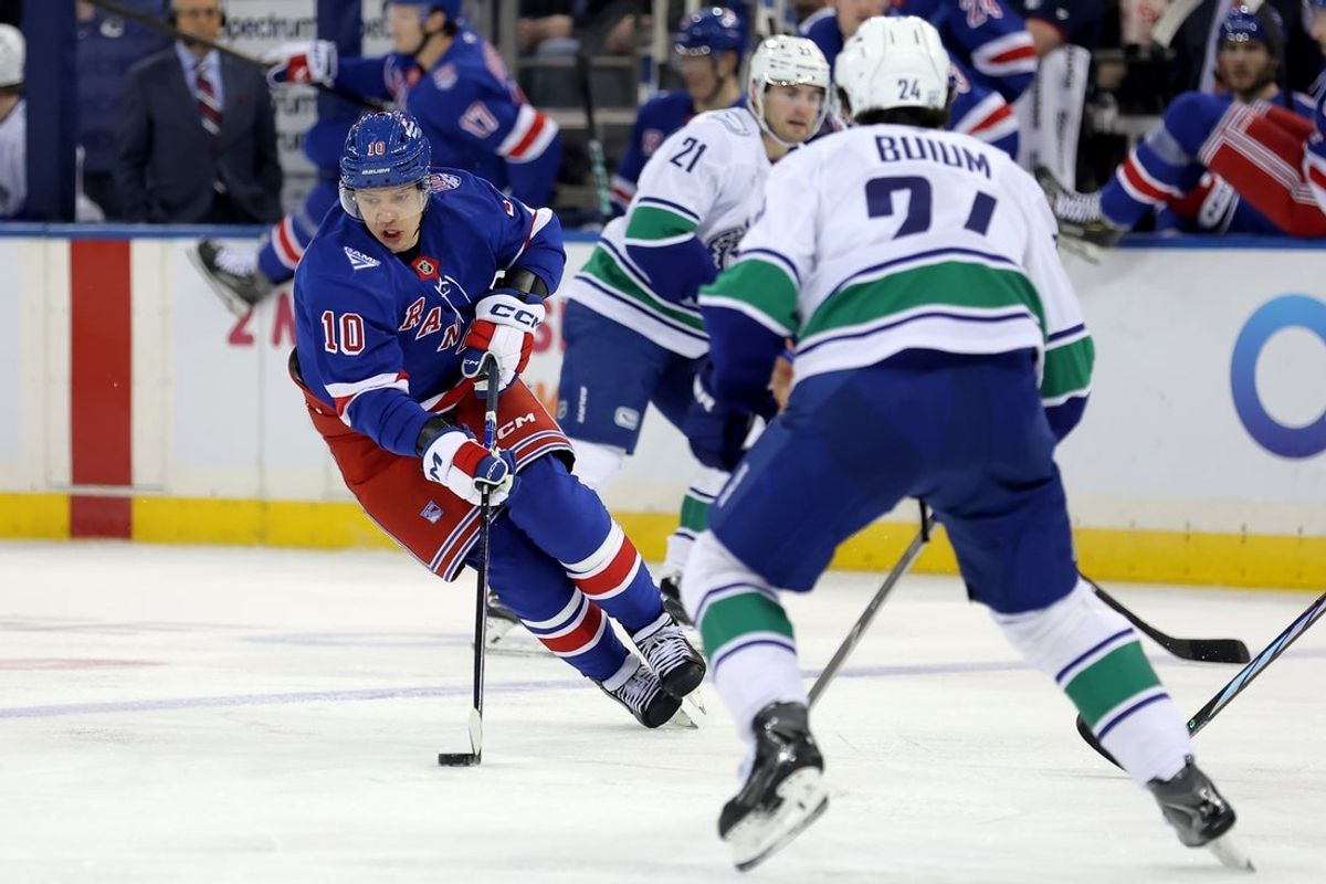 Dec 16, 2025; New York, New York, USA; New York Rangers left wing Artemi Panarin (10) skates with the puck between Vancouver Canucks left wing Nils Hoglander (21) and defenseman Zeev Buium (24) during the second period at Madison Square Garden. Mandatory Credit: Brad Penner-Imagn Images