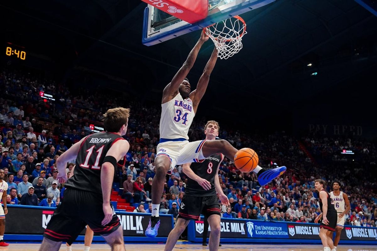 Dec 22, 2025; Lawrence, Kansas, USA; Kansas Jayhawks center Paul Mbiya (34) dunks the ball as Davidson Wildcats guard Sam Brown (11) and guard Joe Hurlburt (8) look on during the second half of the game at Allen Fieldhouse. Mandatory Credit: Denny Medley-Imagn Images