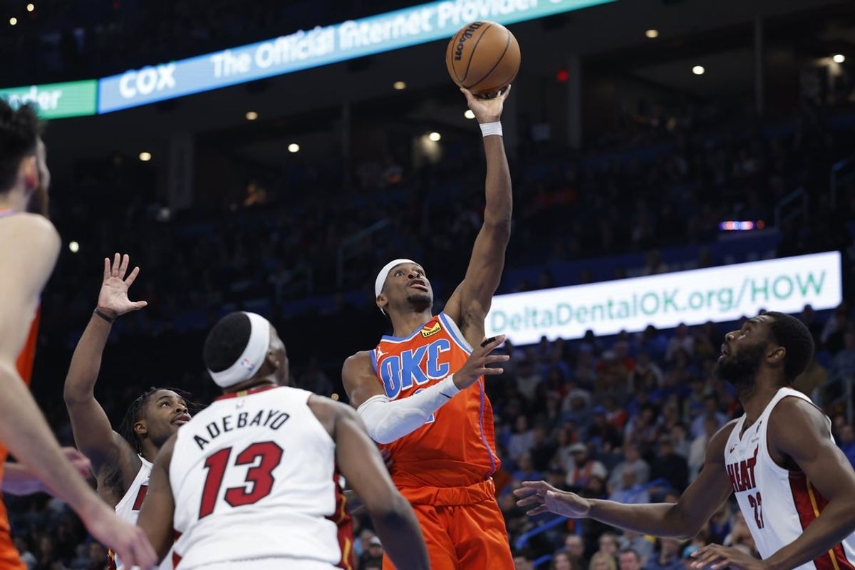 Jan 11, 2026; Oklahoma City, Oklahoma, USA; Oklahoma City Thunder guard Shai Gilgeous-Alexander (2) shoots from between Miami Heat center/forward Bam Adebayo (13) forward Andrew Wiggins (22) during the second half at Paycom Center. Mandatory Credit: Alonzo Adams-Imagn Images