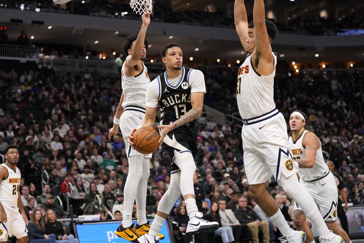 Jan 23, 2026; Milwaukee, Wisconsin, USA;  Milwaukee Bucks guard Ryan Rollins (13) passes the ball around Denver Nuggets forward Spencer Jones (21) during the second quarter at Fiserv Forum. Mandatory Credit: Jeff Hanisch-Imagn Images