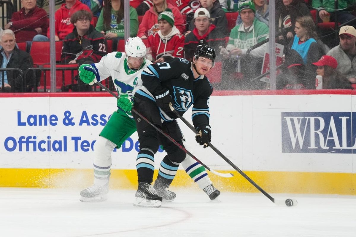 Jan 29, 2026; Raleigh, North Carolina, USA;  Utah Mammoth center Barrett Hayton (27) truest control the pcyuk against Carolina Hurricanes center Jordan Staal (11) during the first period at Lenovo Center. Mandatory Credit: James Guillory-Imagn Images
