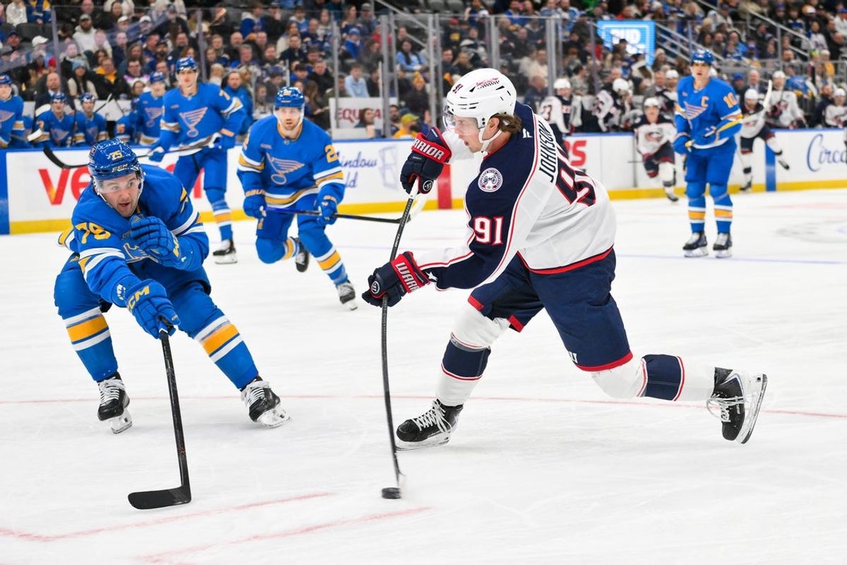 Jan 31, 2026; St. Louis, Missouri, USA; Columbus Blue Jackets center Kent Johnson (91) shoots as St. Louis Blues defenseman Tyler Tucker (75) defends during the first period at Enterprise Center. Mandatory Credit: Jeff Curry-Imagn Images