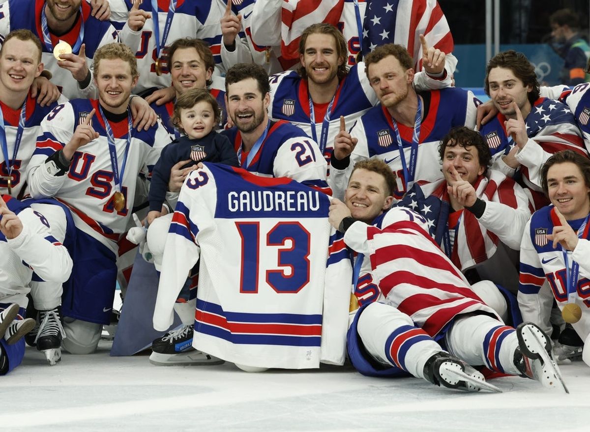 Feb 22, 2026; Milan, Italy; United States players celebrate with a team photo while holding the jersey of Johnny Gaudreau after defeating Canada in the men's ice hockey gold medal game during the Milano Cortina 2026 Olympic Winter Games at Milano Santagiulia Ice Hockey Arena. Mandatory Credit: Geoff Burke-Imagn Images
