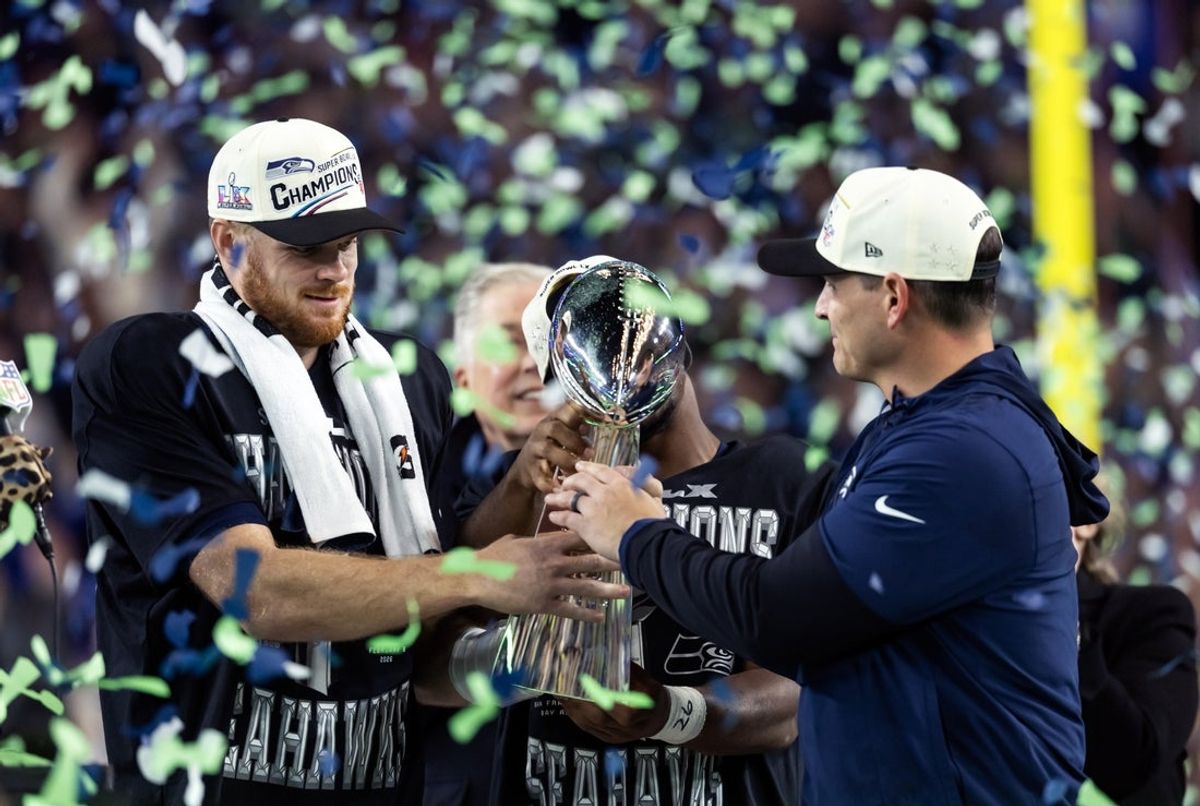 Feb 8, 2026; Santa Clara, CA, USA; Seattle Seahawks head coach Mike MacDonald and quarterback Sam Darnold (14) celebrate with the Vince Lombardi trophy on the podium after defeating the New England Patriots in Super Bowl LX at Levi's Stadium. Mandatory Credit: Mark J. Rebilas-Imagn Images