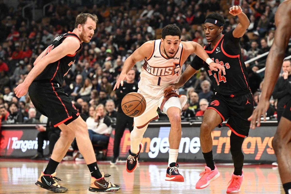 Mar 13, 2026; Toronto, Ontario, CAN;  Phoenix Suns guard Devin Booker (1) dribbles the ball between Toronto Raptors guard Ja'Kobe Walter (14) and center Jakob Poeltl (19) in the first half at Scotiabank Arena. Mandatory Credit: Dan Hamilton-Imagn Images