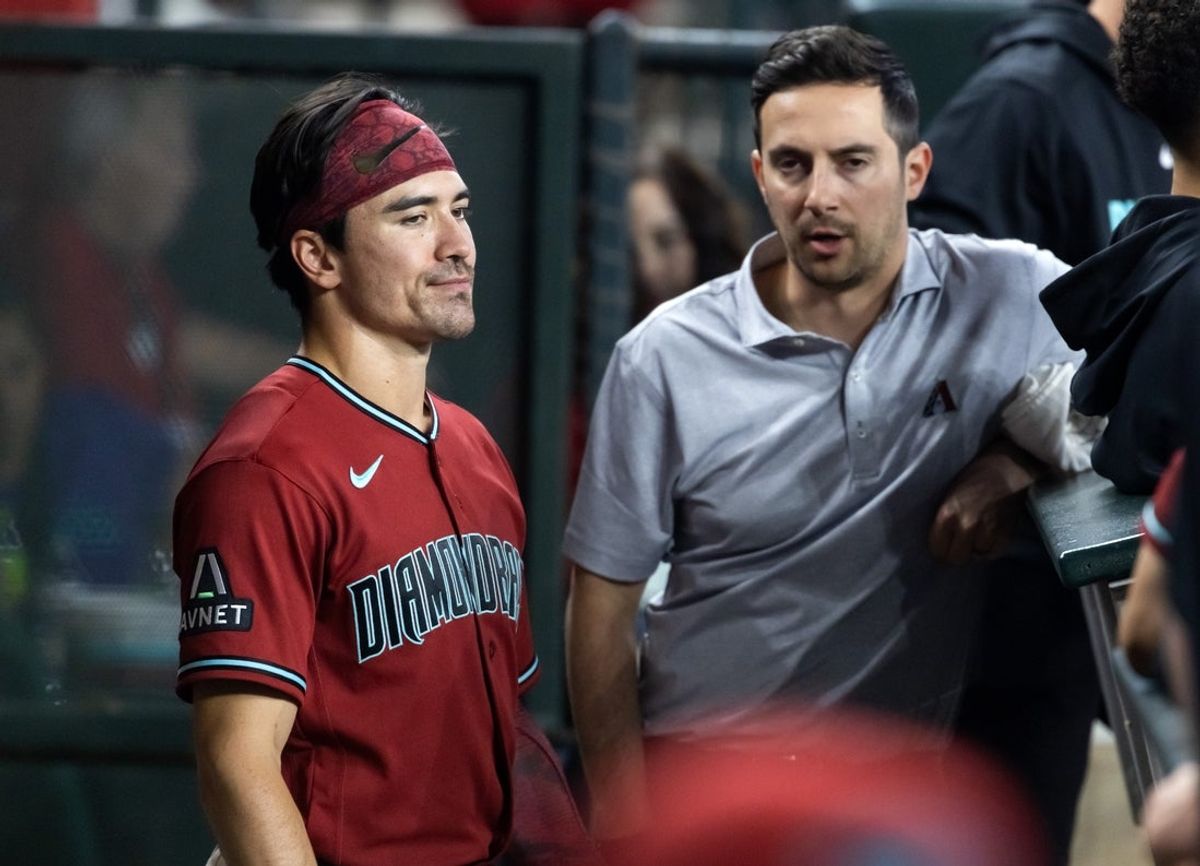 Apr 19, 2026; Phoenix, Arizona, USA; Arizona Diamondbacks outfielder Corbin Carroll (left) talks with a team trainer in the dugout in the fourth inning against the Toronto Blue Jays at Chase Field. Mandatory Credit: Mark J. Rebilas-Imagn Images