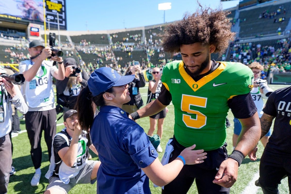 Serena Acosta, left, of the United States Coast Guard, exchanges a gift with Oregon quarterback Dante Moore following the Oregon Ducks annual spring game on April 25, 2026 at Autzen Stadium in Eugene, Oregon.