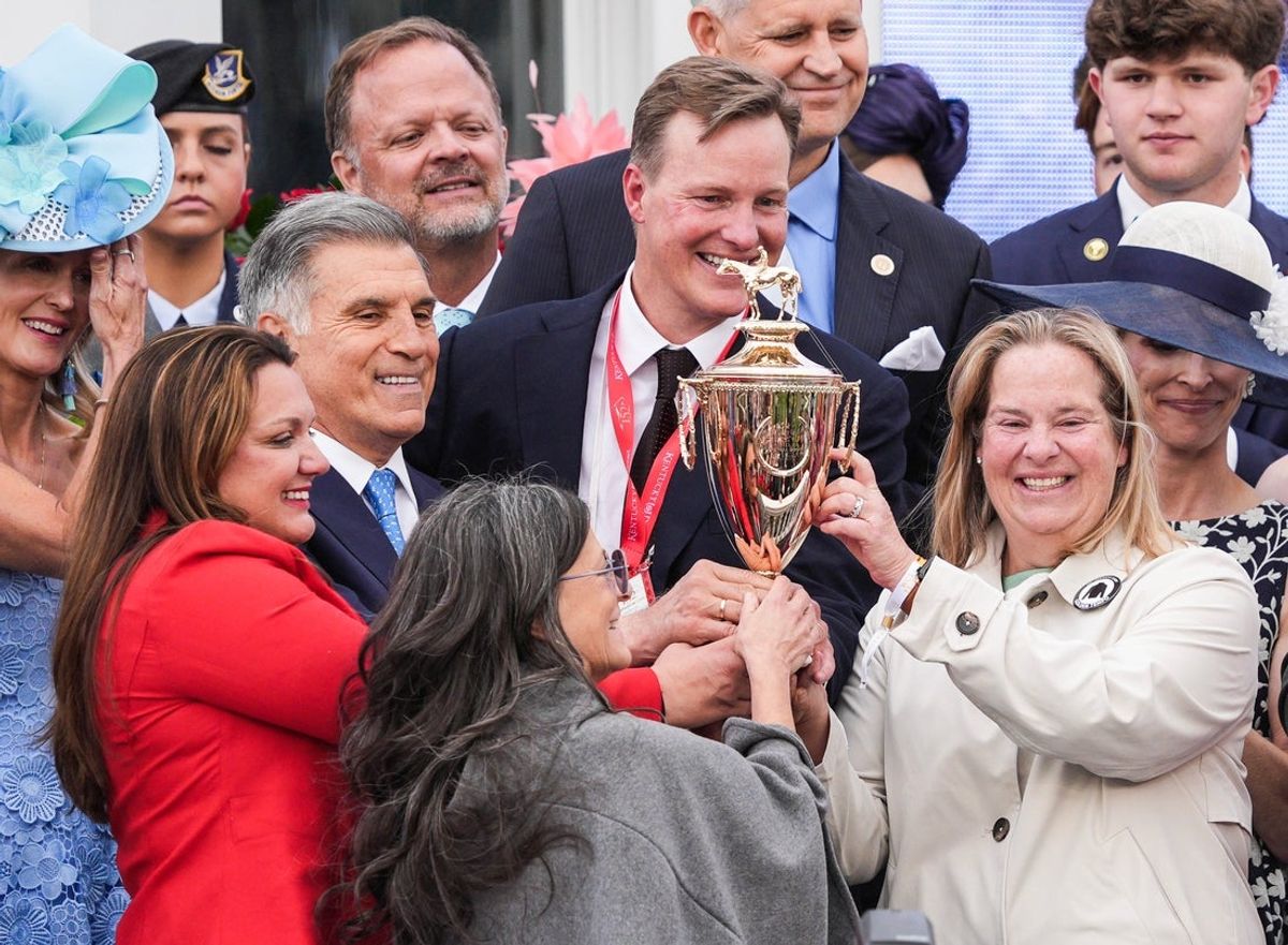 Trainer Cherie DeVaux, in red jacket at left, helps lift the Kentucky Derby trophy with Daisy Phipps Pulito (representing Phipps Stable) and Vincent Viola (of St. Elias Stable) after Golden Tempo won the 2026 Kentucky Derby. May 2, 2026.