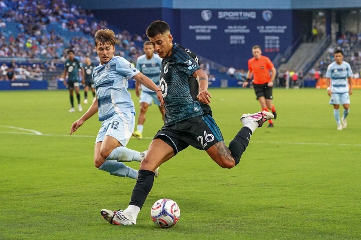 Jul 22, 2026; Kansas City, Kansas, USA; Minnesota United FC midfield Joaquín Pereyra (26) kicks a shot on goal as Sporting Kansas City midfield Jake Davis (8) defends during the first half of the match at Children's Mercy Park. Mandatory Credit: Denny Medley-Imagn Images