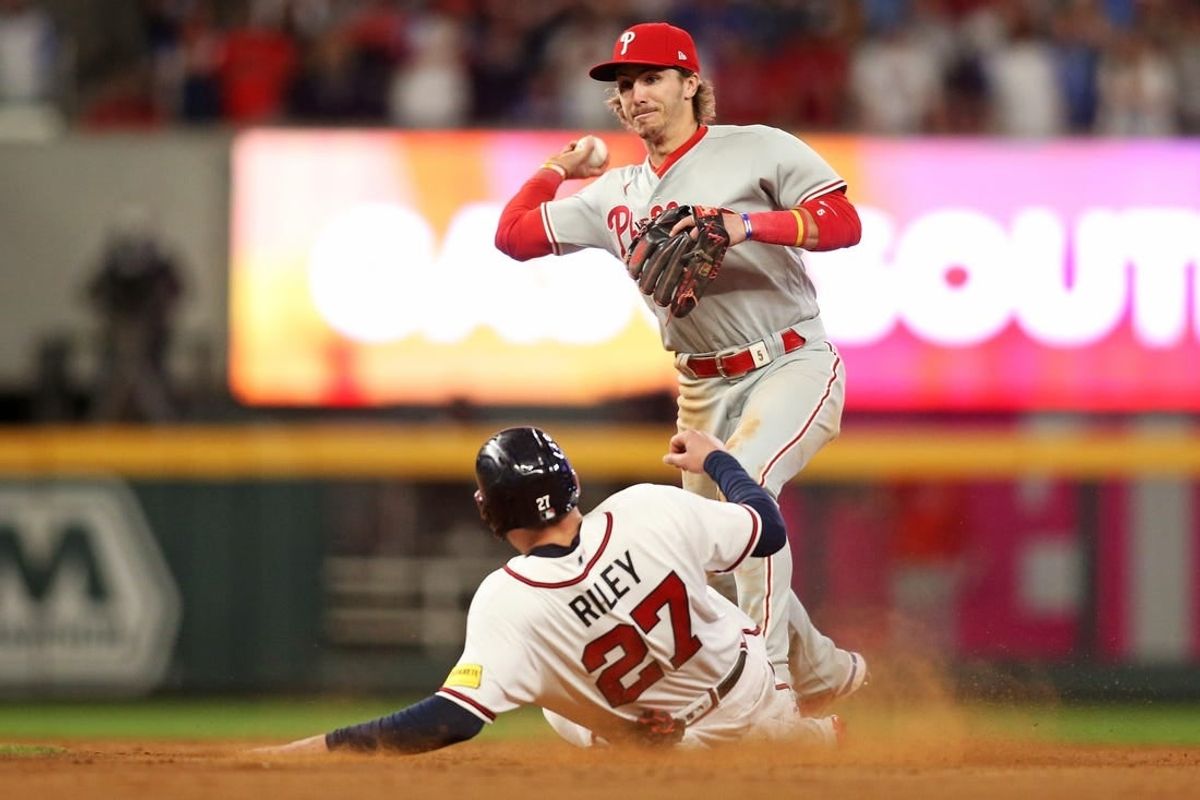 Oct 7, 2023; Cumberland, Georgia, USA; Philadelphia Phillies second baseman Bryson Stott (5) turns a double play over Atlanta Braves third baseman Austin Riley (27) during the eighth inning during game one of the NLDS for the 2023 MLB playoffs at Truist Park.