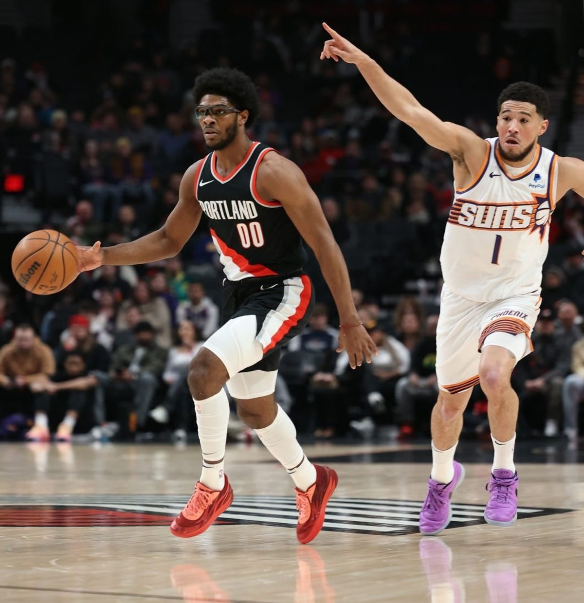 Jan 14, 2024; Portland, Oregon, USA; Portland Trail Blazers guard Scoot Henderson (00) dribbles the ball as Phoenix Suns guard Devin Booker (1) directs traffic in the first quarter at Moda Center.