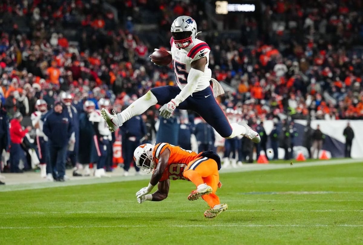 Dec 24, 2023; Denver, Colorado, USA; New England Patriots running back Ezekiel Elliott (15) jumps over Denver Broncos cornerback Ja'Quan McMillian (29) in the third quarter at Empower Field at Mile High.