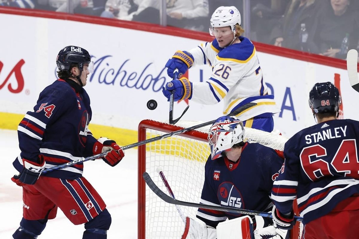 Nov 17, 2023; Winnipeg, Manitoba, CAN; Winnipeg Jets defenseman Dylan Samberg (54) and Buffalo Sabres defenseman Rasmus Dahlin (26) bat at the puck behind Winnipeg Jets goaltender Connor Hellebuyck (37) in the third period at Canada Life Centre.