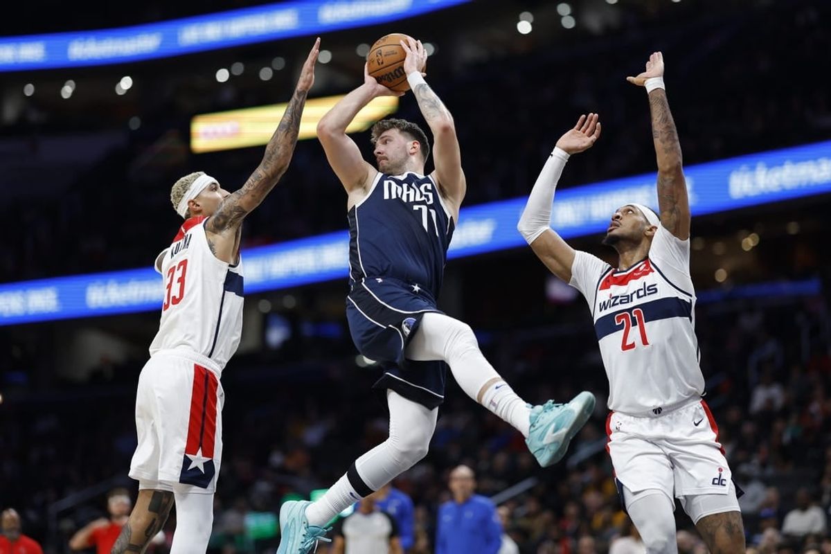 Nov 15, 2023; Washington, District of Columbia, USA; Dallas Mavericks guard Luka Doncic (77) leaps to pass the ball as Washington Wizards forward Kyle Kuzma (33) and Wizards center Daniel Gafford (21) defend in the first quarter at Capital One Arena.