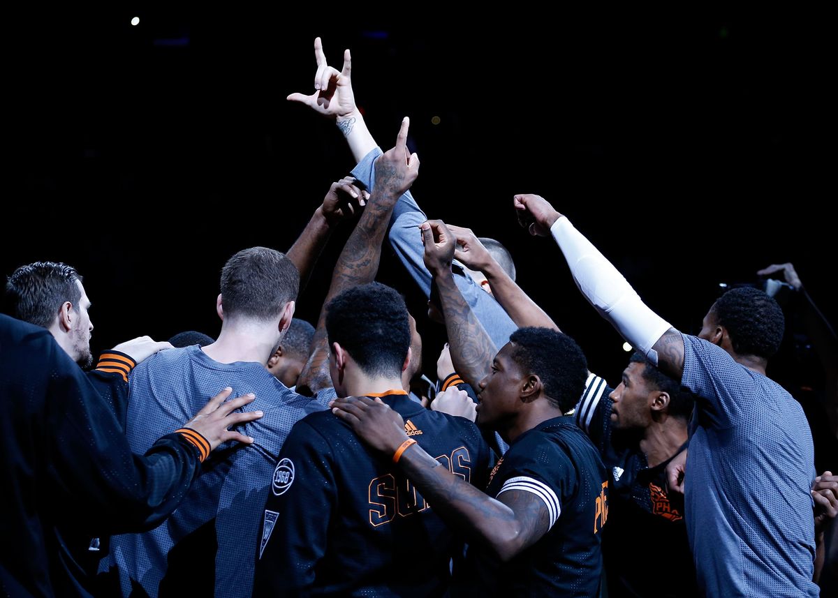 The Phoenix Suns, still dressed in pregame warmups, raise their fists in the air in a huddle before the start of an NBA game.