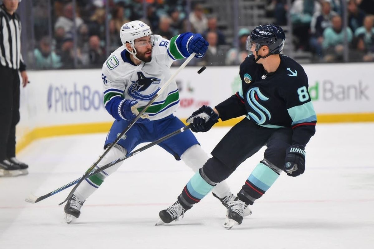 Nov 24, 2023; Seattle, Washington, USA; Vancouver Canucks defenseman Mark Friedman (51) and Seattle Kraken defenseman Brian Dumoulin (8) play the puck during the first period at Climate Pledge Arena.