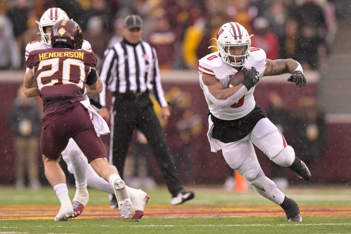 Nov 25, 2023; Minneapolis, Minnesota, USA;  Wisconsin Badgers running back Braelon Allen (0) runs with the ball as quarterback Tanner Mordecai (8) puts a block on Minnesota Golden Gophers defensive back Jack Henderson (20) at Huntington Bank Stadium.