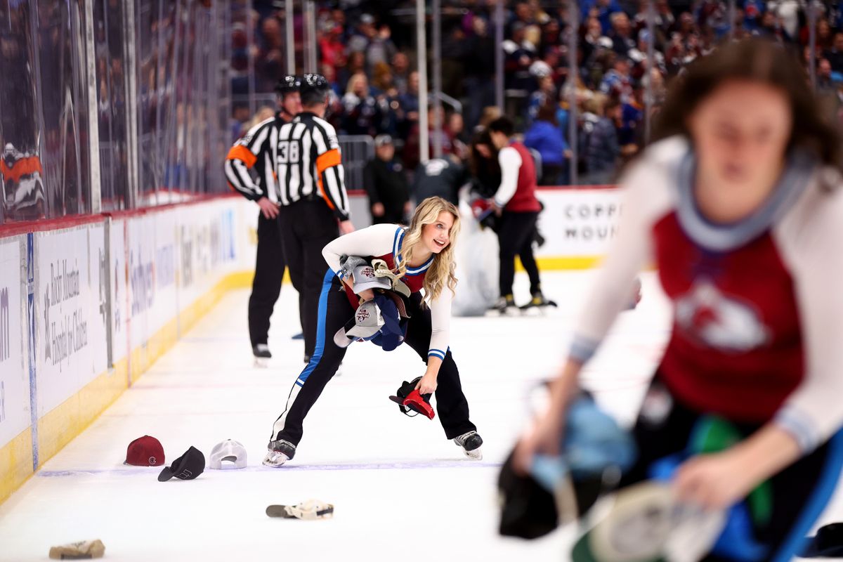 Avalanche employees remove hats and other “garments” from ice after Nathan Mackinnon’s fourth goal Wednesday night.