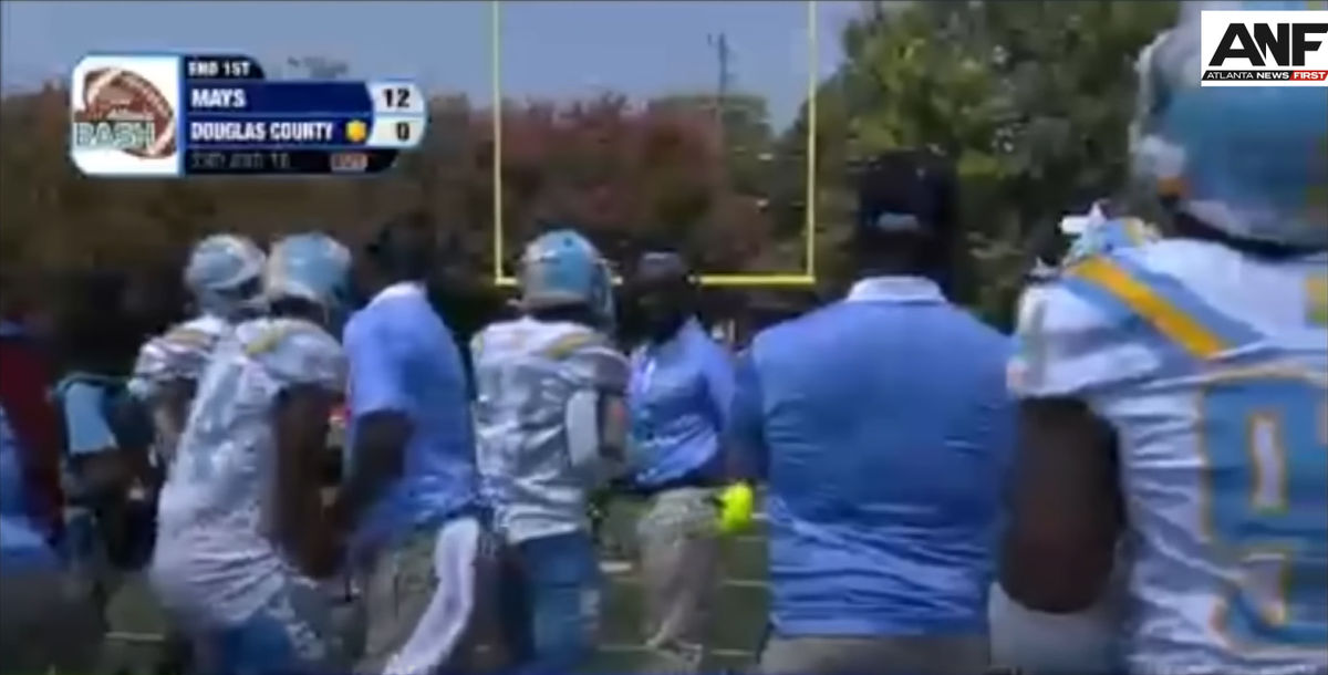 The coach can be seen toward the left side of the frame striking a player in the gut.