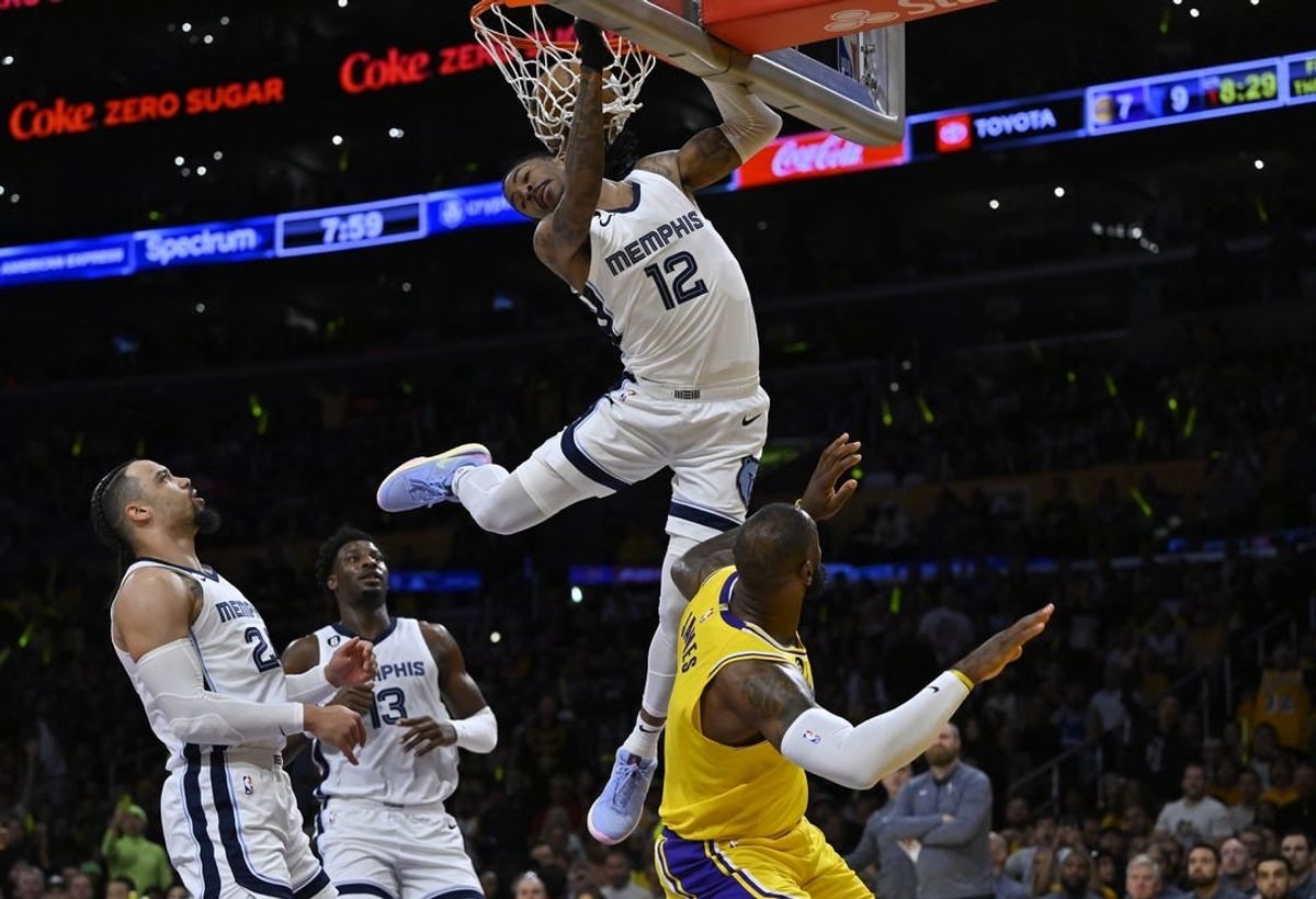 Apr 28, 2023; Los Angeles, California, USA; Memphis Grizzlies guard Ja Morant (12) hangs on the rim to avoid landing on Los Angeles Lakers forward LeBron James (6) after a dunk in the first quarter of game six of the 2023 NBA playoffs at Crypto.com Arena.