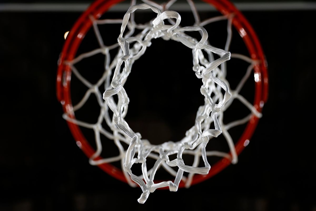 A red basketball hoop with a white net is shown from below against a black background.