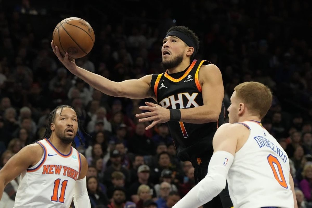 Dec 15, 2023; Phoenix, Arizona, USA; Phoenix Suns guard Devin Booker (1) drives between New York Knicks guard Jalen Brunson (11) and  guard Donte DiVincenzo (0) in the first half at Footprint Center.