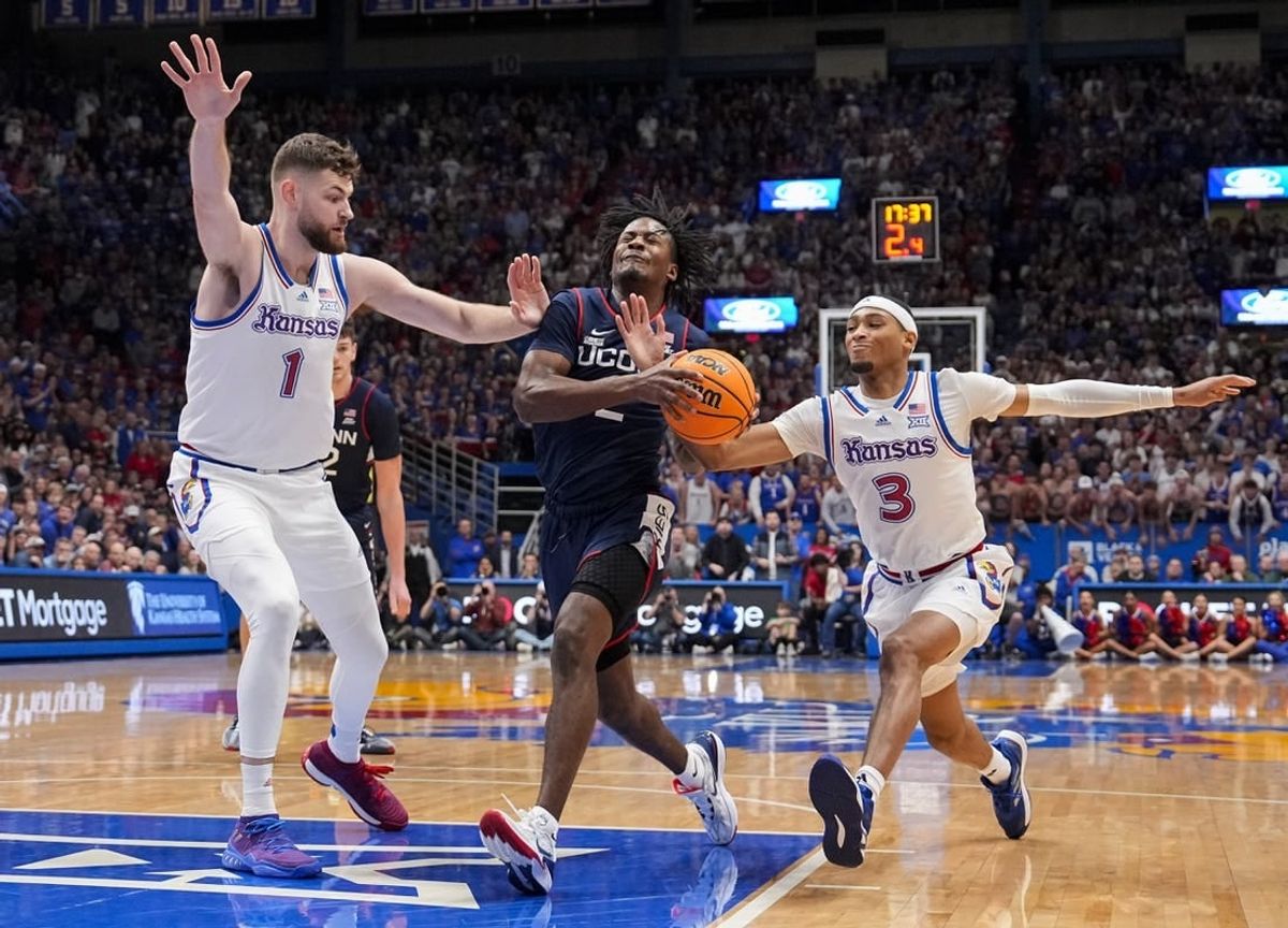 Dec 1, 2023; Lawrence, Kansas, USA; Connecticut Huskies guard Tristen Newton (2) drives against Kansas Jayhawks center Hunter Dickinson (1) and guard Dajuan Harris Jr. (3) during the first half at Allen Fieldhouse.