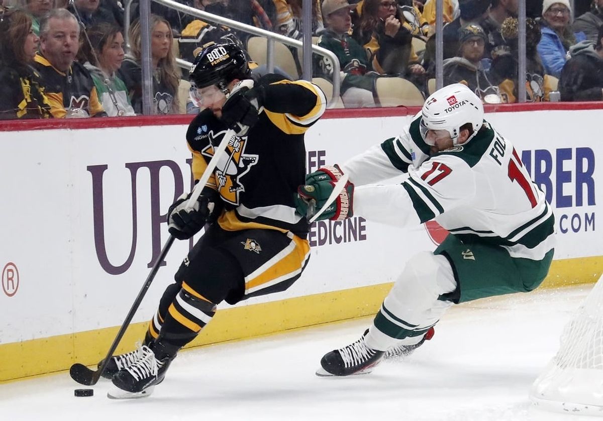 Dec 18, 2023; Pittsburgh, Pennsylvania, USA;  Pittsburgh Penguins defenseman Kris Letang (58) handles the puck against pressure from Minnesota Wild left wing Marcus Foligno (17) during the first period at PPG Paints Arena.