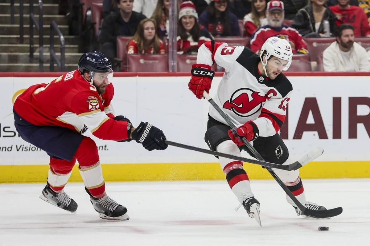 Jan 13, 2024; Sunrise, Florida, USA; New Jersey Devils center Nico Hischier (13) protects the puck from Florida Panthers defenseman Aaron Ekblad (5) during the first period at Amerant Bank Arena.