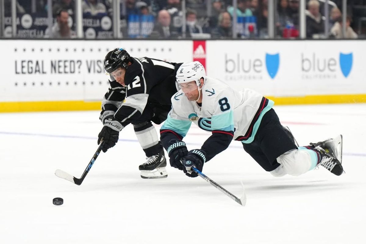 Dec 20, 2023; Los Angeles, California, USA; Seattle Kraken defenseman Brian Dumoulin (8) and LA Kings left wing Trevor Moore (12) reach for the puck in the second period at Crypto.com Arena.