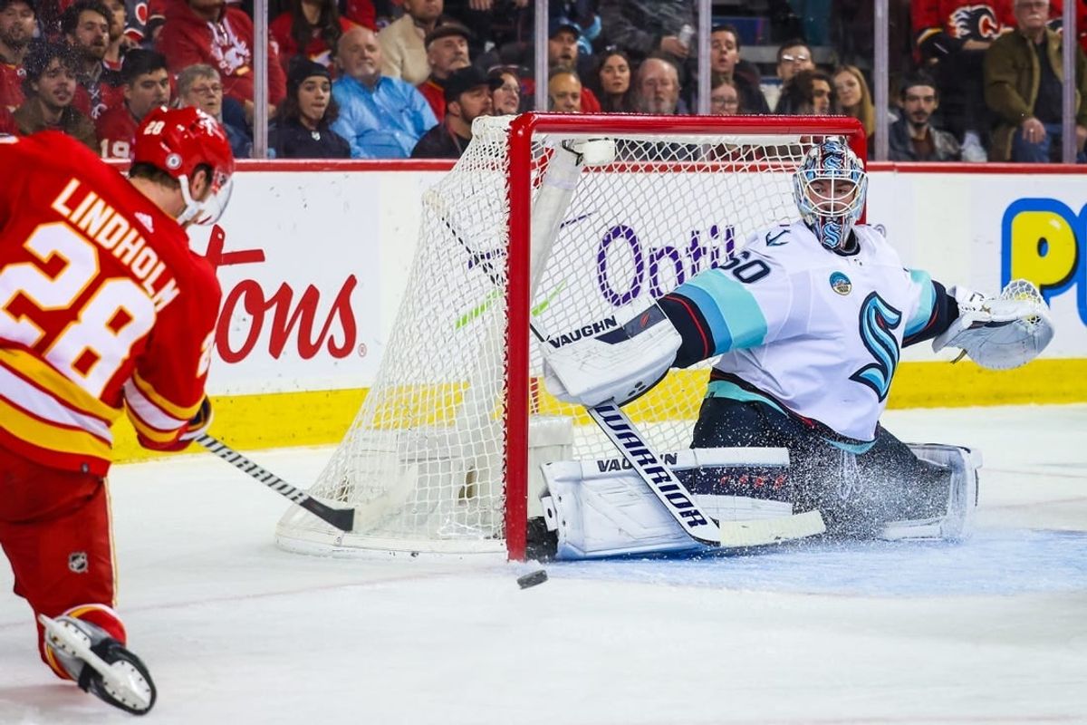 Dec 27, 2023; Calgary, Alberta, CAN; Seattle Kraken goaltender Chris Driedger (60) makes a save against Calgary Flames center Elias Lindholm (28) during the second period at Scotiabank Saddledome.