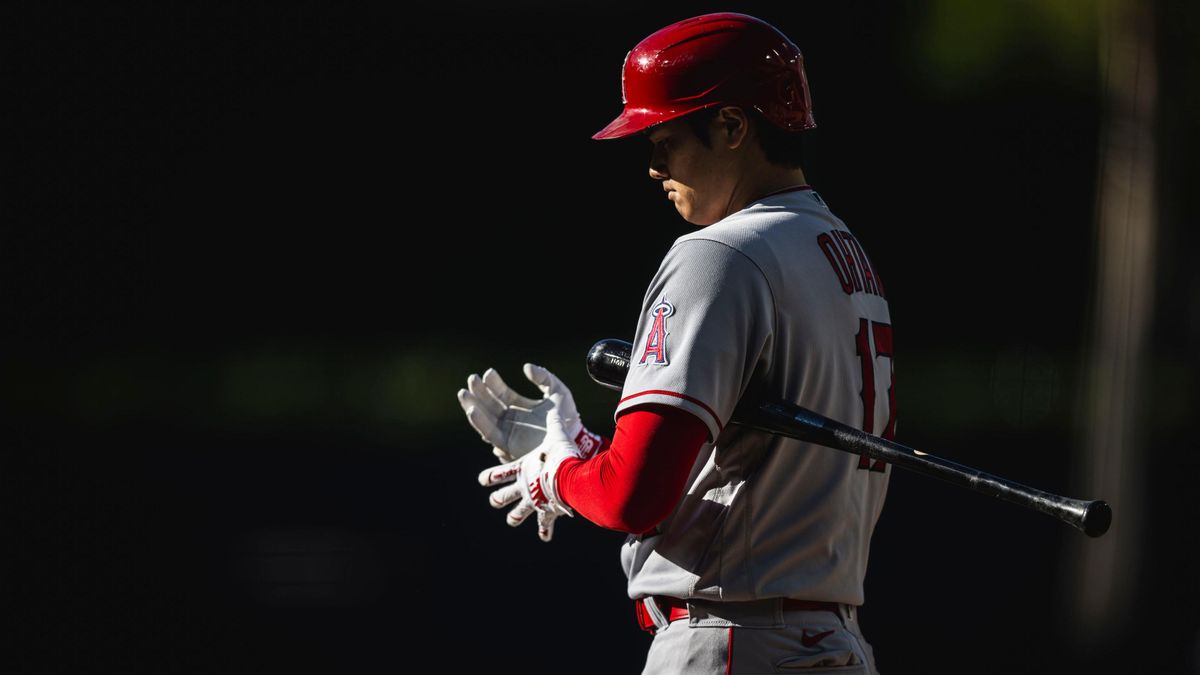 An Asian man in a gray and red baseball uniform adjusts his batting gloves while holding a black baseball bat under his arm.