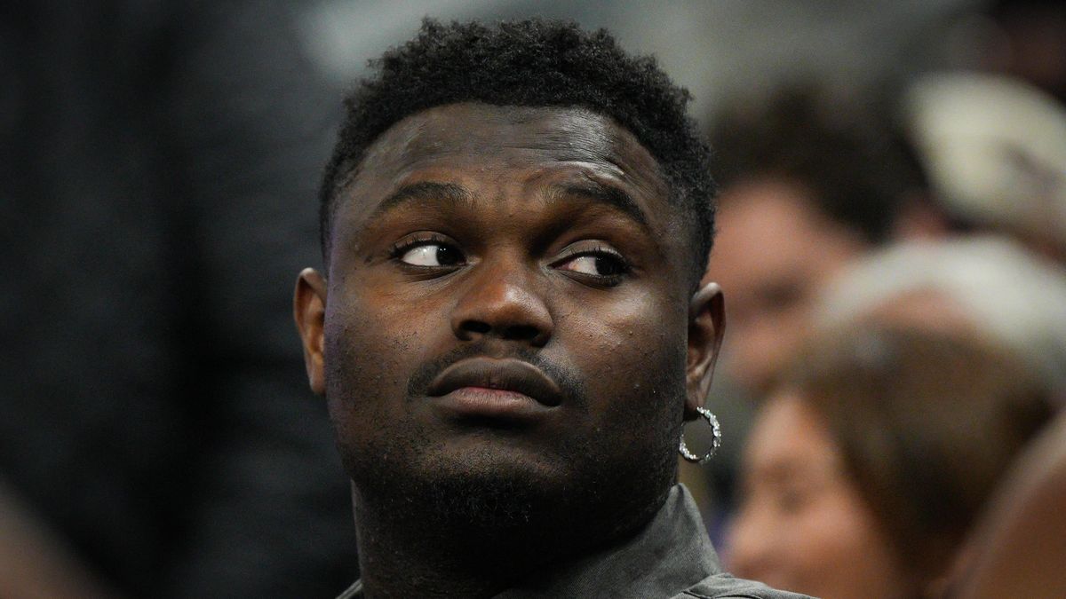 A close up of NBA star Zion Williamson, looking contemplative, in street clothes from the bench while watching his teammates take on Golden State.