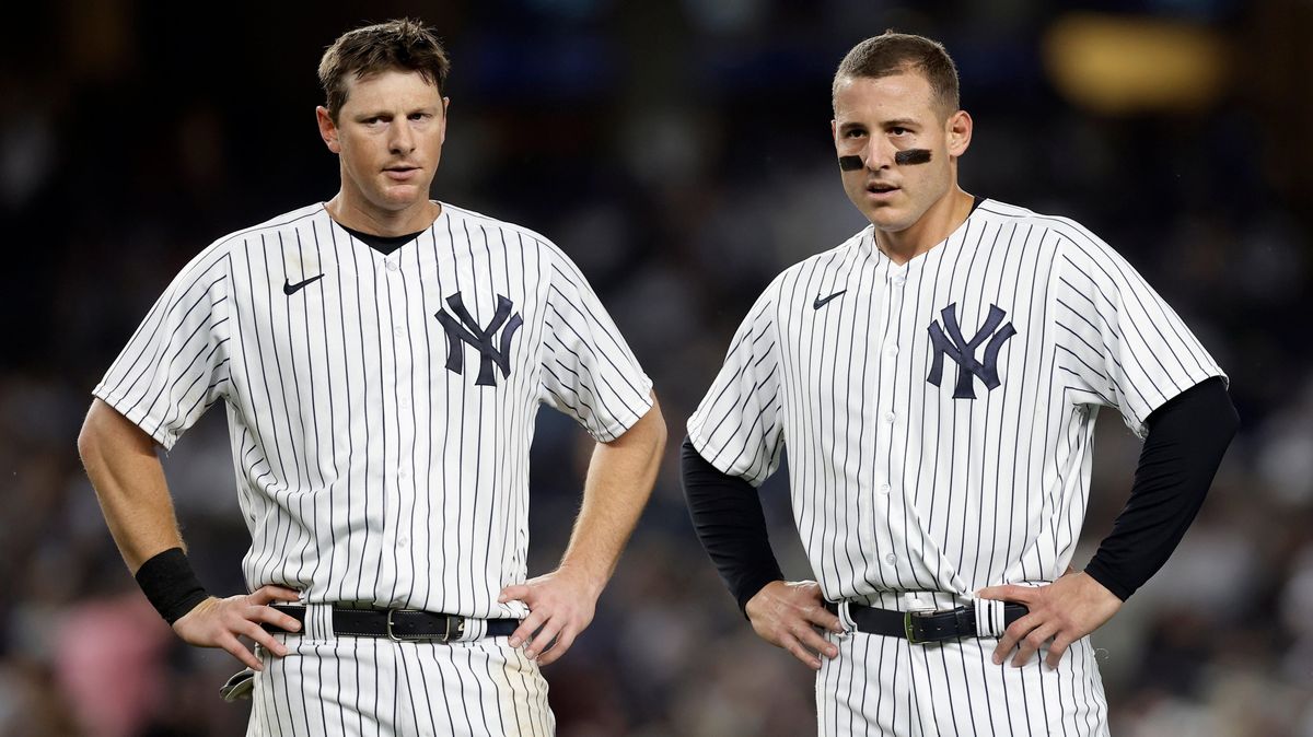 Two white men in white baseball uniforms with blue pinstripes stand with their hands on their hips during an MLB baseball game.