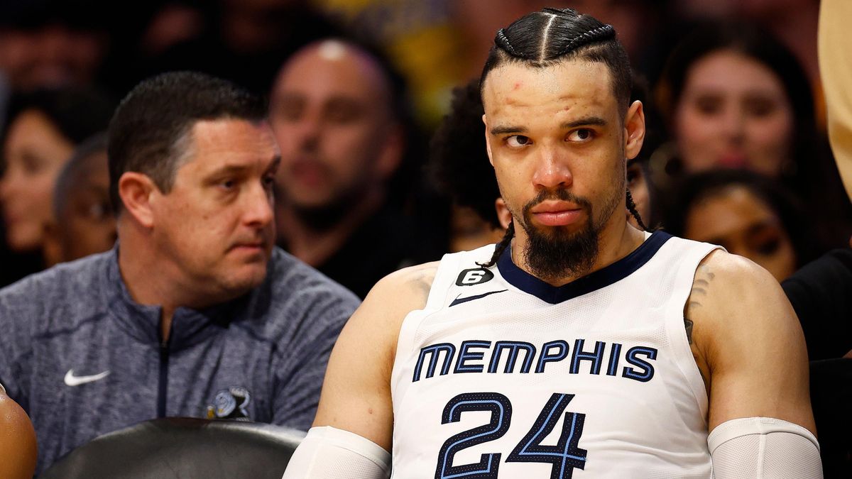 A Black man with his hair in braids and a goatee sits on the sidelines of an NBA basketball game, wearing a white jersey that says "Memphis" across the chest.